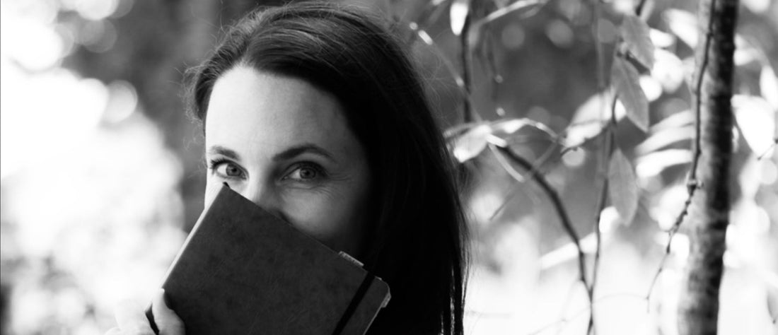 Die Autorin und Keramikerin Serena Maria Zimmermann hält ein Notizbuch teils über ihr Gesicht, im Hintergrund sind Bäume.